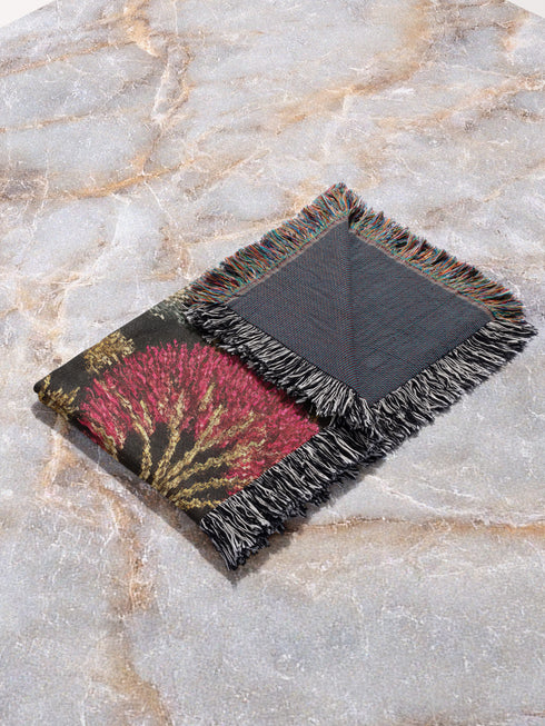 Jacquard-woven cotton blanket featuring twin celestial suns—two serene faces meeting at center—with radiant golden rays on a charcoal ground, bordered by folkloric botanicals and fan blossoms in sage, sky, and garnet. Crafted from 100% soft cotton yarn; the artwork is woven, not printed. Reversible with a color-negative back and finished with a protective 2-inch multicolor fringe. Sizes: 52×37, 50×60, 60×80 for wall, sofa, or queen-bed layering.